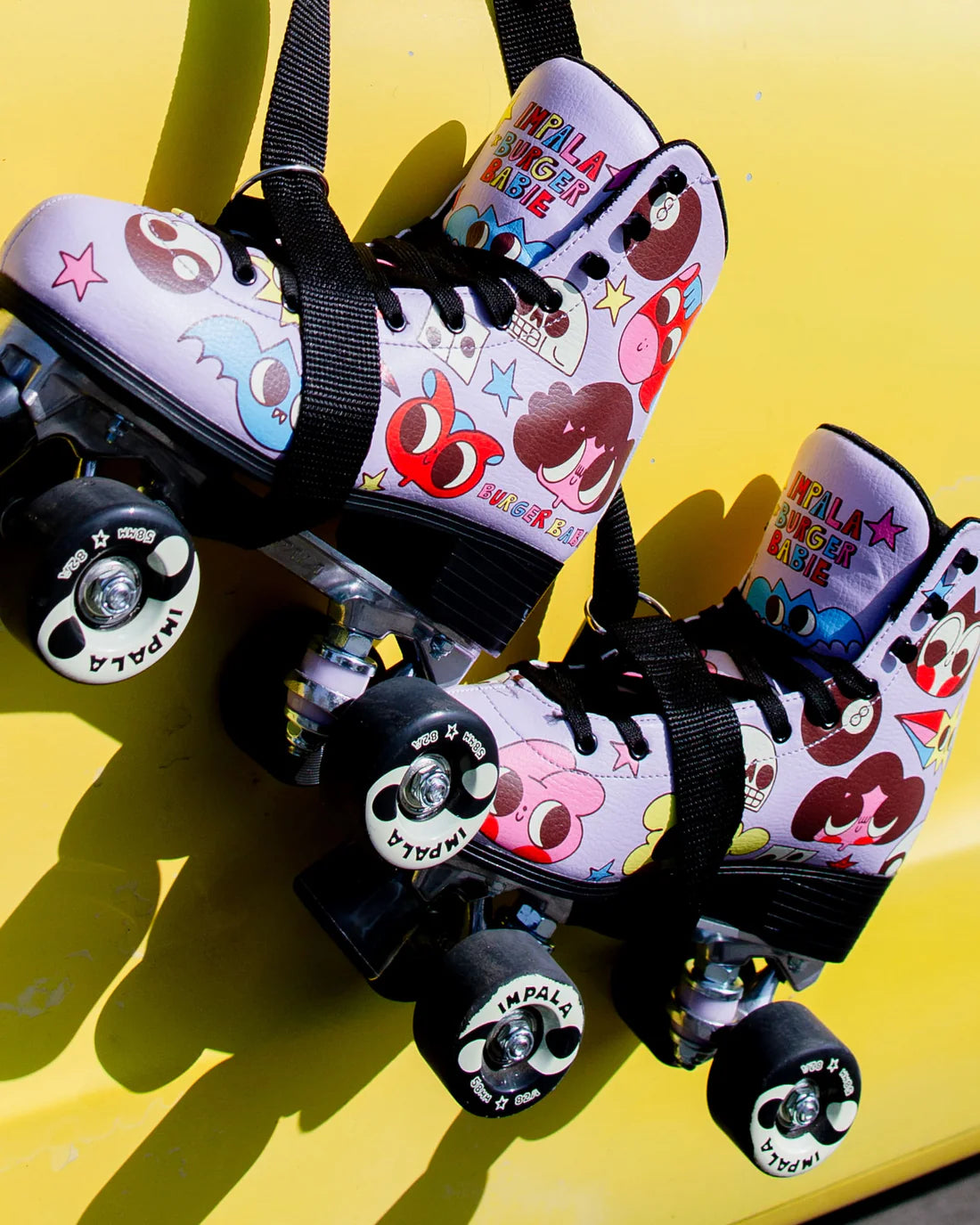 Pink rollerskates with cartoons, hanging in front of a yellow wall ￼