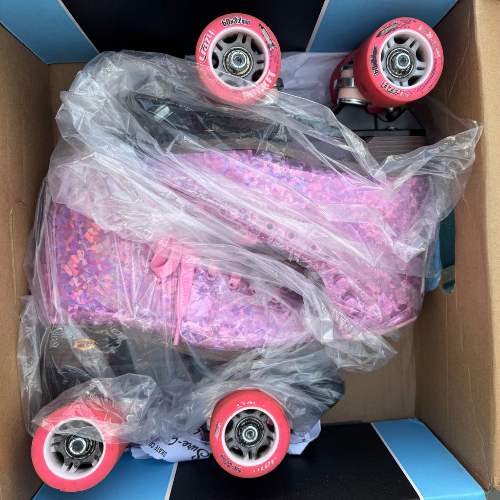Pink roller skates with red wheels in a cardboard box