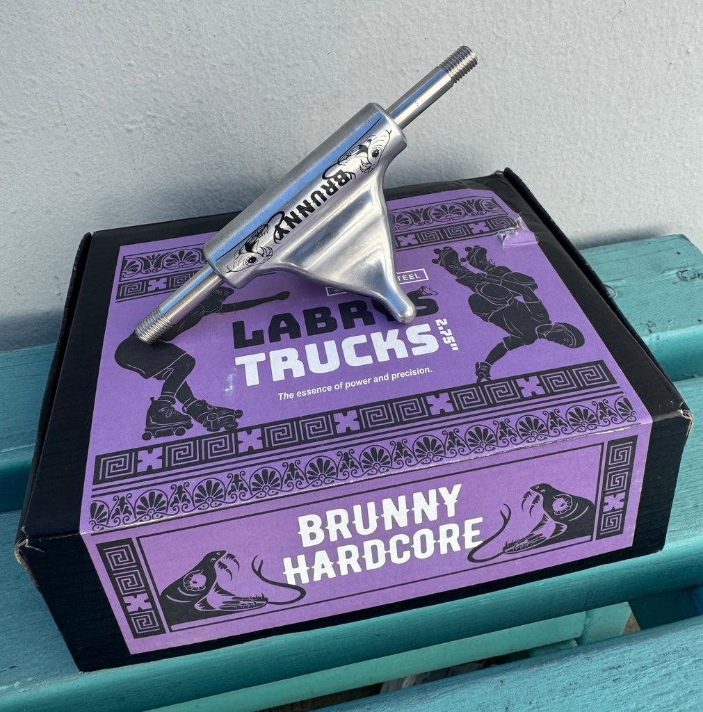 Purple and black skateboard truck box with a silver truck on a light blue surface