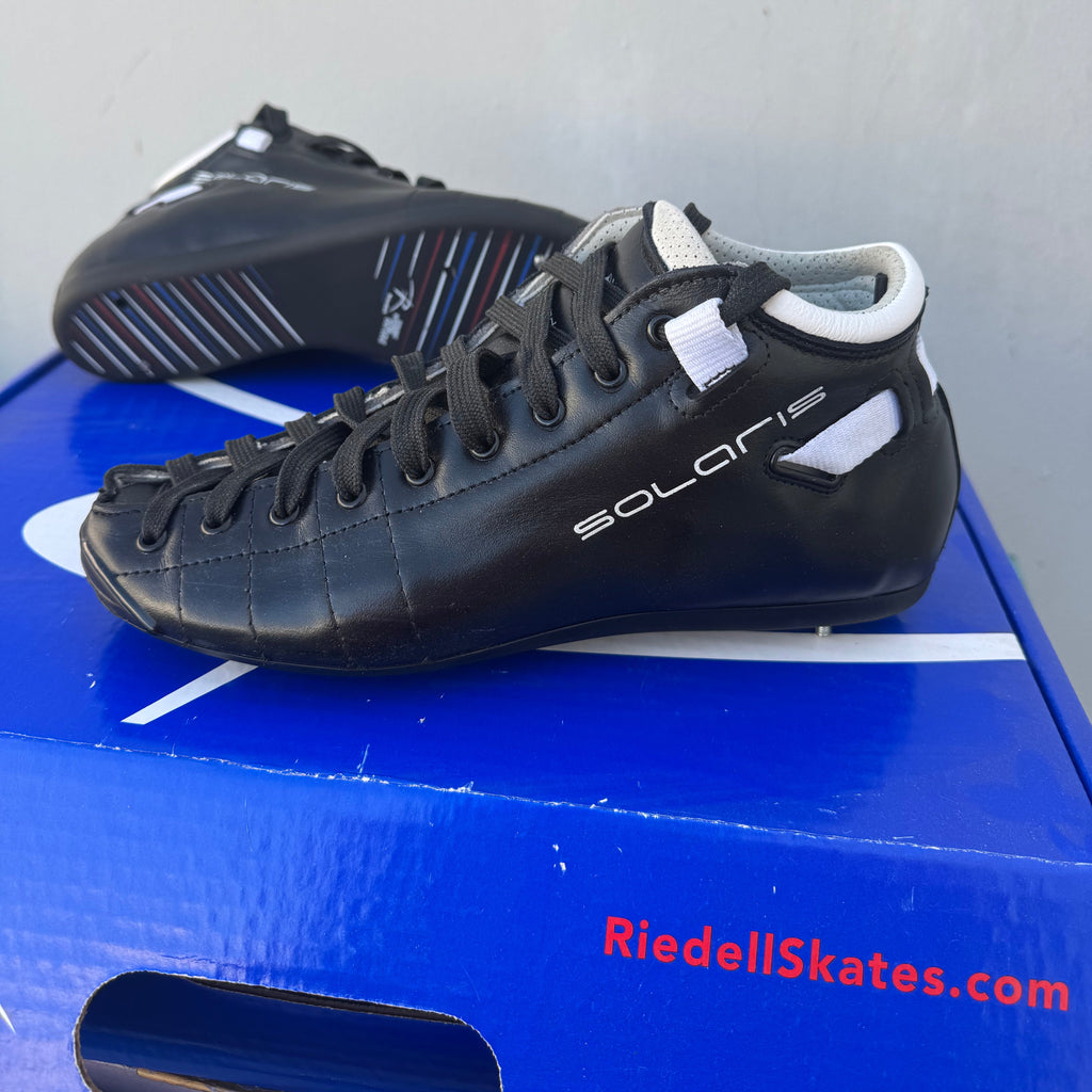 Black ice skate leaning against a blue board with 'RiedellSkates.com' text.