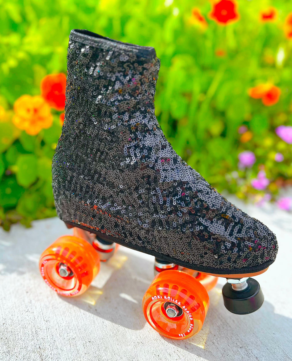 A roller skate boot cover covered in black sequins, displayed on a roller skate with orange wheels.