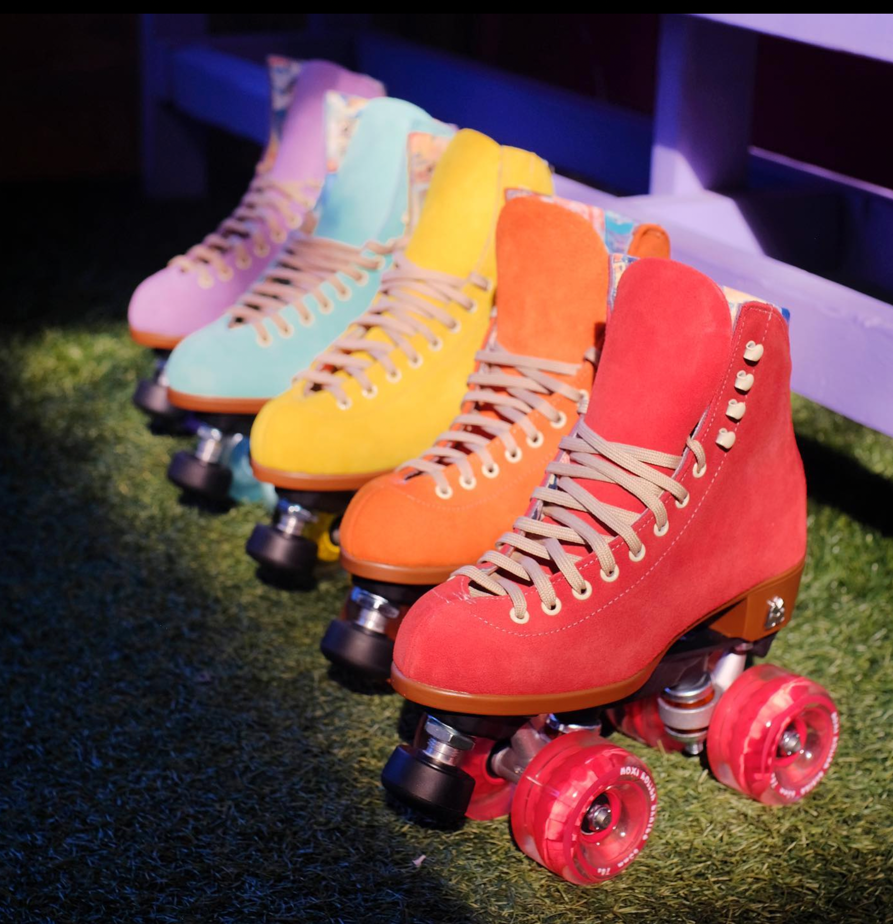 Moxi Lolly Roller Skates in a rown, purple, blue, yellow, orange and red, on fake grass.